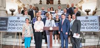 Crowd of people in front of a podium with signs reading, "Working Together for Good."